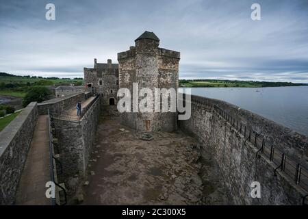 Ein männlicher Tourist steht auf dem Balkon mit Blick auf Blackness Castle, geformt wie ein Schiff, während er Filmorte des beliebten Zeitreiseausländers besucht Stockfoto