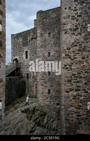 Eine weibliche Touristin spaziert über den felsigen Fuß des Blackness Castle, geformt wie ein Schiff, während sie Filmorte des beliebten Zeitfahrens Outlander tv besucht Stockfoto