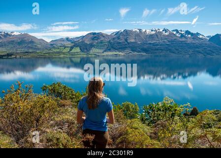 Junge Frau, die über den Wakatipu-See blickt, Berge, die sich im See spiegeln, Otago, Südinsel, Neuseeland Stockfoto