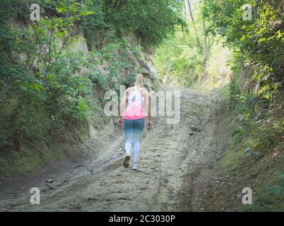 Junge Blonde kaukasische Frau zu Fuß in Wald auf einer Feldstraße Stockfoto