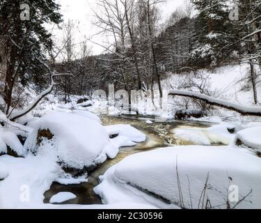 Eiskalt kleiner Fluss. Banken mit Bäumen bedeckt mit Schnee Stockfoto