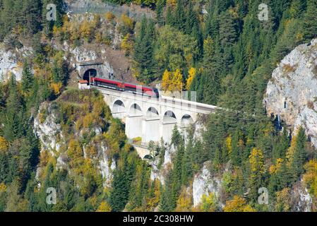 Roter Zug auf einem Viadukt zwischen zwei Tunneln der Semmeringbahn. Die Semmeringbahn ist die älteste Bergbahn Europas und gehört zur UNESCO-Welt Stockfoto