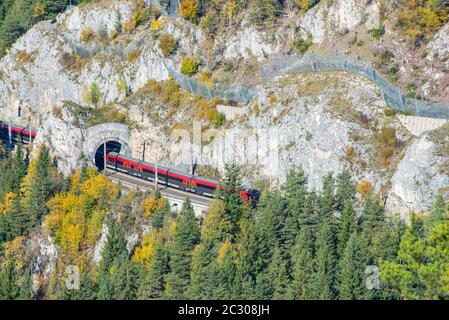 Roter Zug auf einem Viadukt zwischen zwei Tunneln der Semmeringbahn. Die Semmeringbahn ist die älteste Bergbahn Europas und gehört zur UNESCO-Welt Stockfoto