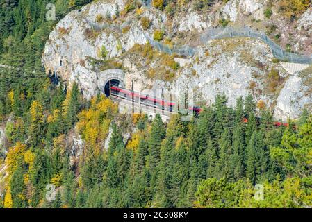 Roter Zug auf einem Viadukt zwischen zwei Tunneln der Semmeringbahn. Die Semmeringbahn ist die älteste Bergbahn Europas und gehört zur UNESCO-Welt Stockfoto