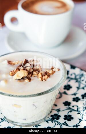 Albanisches traditionelles Joghurt-Dessert mit Honig und Walnüssen über weißem Teller Cappuccino Kaffee im Hintergrund Stockfoto