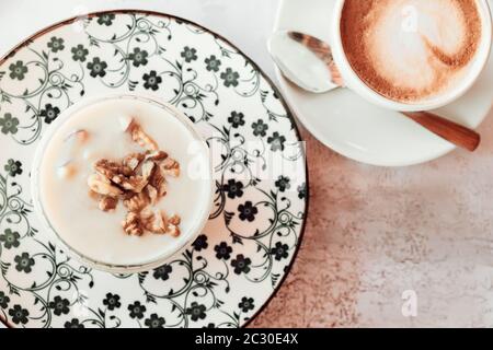 Albanisches traditionelles Joghurt-Dessert mit Honig und Walnüssen über weißem Teller Cappuccino Kaffee Draufsicht Stockfoto