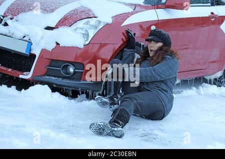 Eine Frau rutschte im Winter aus und fiel vor ein Auto. Gefahr im winterlichen Straßenverkehr Stockfoto