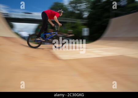 BMX-Fahrer springt auf einer U-Rampe in einem Skatepark über (Bewegungsunschärfe) Stockfoto