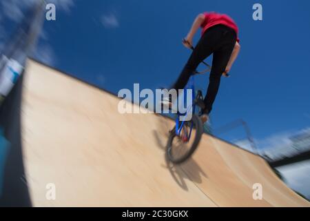 BMX-Fahrer springt auf einer U-Rampe in einem Skatepark über (Bewegungsunschärfe) Stockfoto