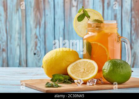Zitruslimonade mit Eis, Minzblättern, Zitronen- und Limettenscheiben stehen auf einem blauen Holztisch. Hausgemachte Limonade mit Zitrusfrüchten. Gesundes kühles Getränk Stockfoto