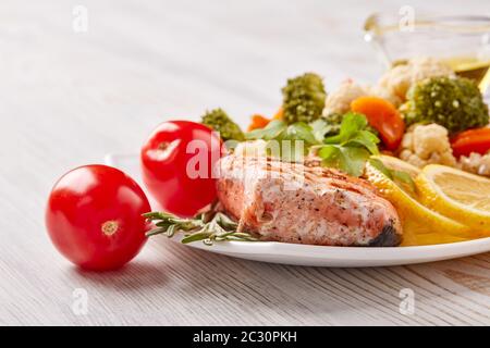 Gegrilltes Lachsfilet garniert mit Gemüse, Zitrone, Tomaten, Kräutern auf dem Teller auf Holzhintergrund. Gesunde Ernährung. Keto-Diät. Stockfoto