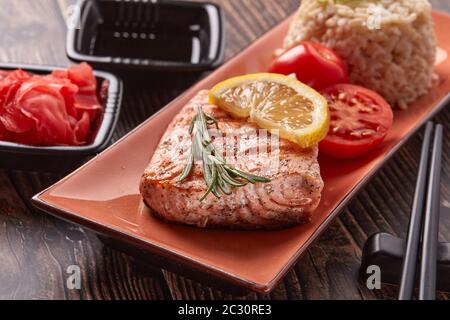 Gegrilltes Lachsfilet mit Reis, eingelegtem Ingwer, Sojasauce, Tomaten, Zitrone und Kräutern auf dunklem Holzhintergrund. Gesunde Ernährung. Stockfoto