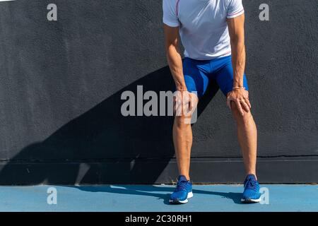 Junger Laufmann in blauer Hose und weißem Hemd, der sich in voller Sonne auf der schwarzen Wand ausruhte und erholte. Motivationskonzept, Karriere Stockfoto