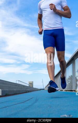 Junger Läufer in blauer Hose und weißem T-Shirt läuft in der Sonne auf blauer Bahn. Motivationskonzept, Karriere Stockfoto