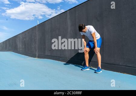 Junger Laufmann in blauer Hose und weißem Hemd, der sich in voller Sonne auf der schwarzen Wand ausruhte und erholte. Motivationskonzept, Karriere Stockfoto