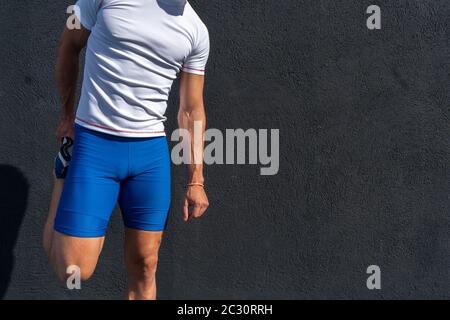 Junger Mann läuft in blauen Hosen und weißen Hemd ruht und erholt sich auf der schwarzen Wand in voller Sonne, dabei Bein Strecken. Motivationskonzept, Karriere Stockfoto