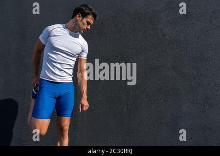 Junger Mann läuft in blauen Hosen und weißen Hemd ruht und erholt sich auf der schwarzen Wand in voller Sonne, dabei Bein Strecken. Motivationskonzept, Karriere Stockfoto
