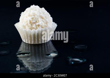 Weiße Schokolade Kokosnusstrüffel auf schwarzem Hintergrund mit schöner Reflexion Stockfoto