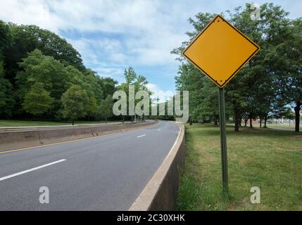 Ein blank gelbes, diamand geformtes Schild an der Seite einer leeren Autobahn mit Bäumen auf beiden Seiten Stockfoto