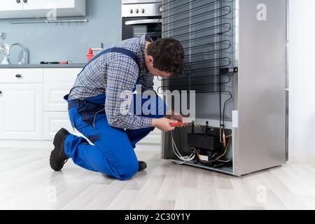 Männliche Arbeiter Instandsetzung Kühlschrank mit Schraubendreher im Haus Stockfoto