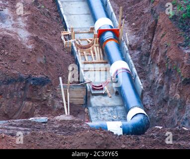 Neue Wasserleitungen werden in Gräben aus Betonkanälen verlegt. Das Konzept der Verlegung von Industriestraßen. Stockfoto