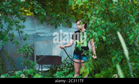 Frau, die den Garten aus dem Schlauch wässert. Weibchen sprühen Wasser auf Gemüse mit einem Gartenschlauch. Eine glückliche Frau mit einem Schlauch kümmert sich um den Garten Stockfoto