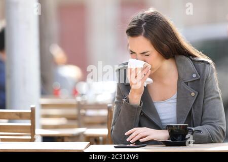 Kranke Frau, die ihre Nase weht und auf einer Terrasse im Café Gewebe sitzt Stockfoto