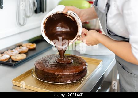 Patissier, die in ihrer Werkstatt flüssige Schokolade auf einen Kuchen gießt Stockfoto