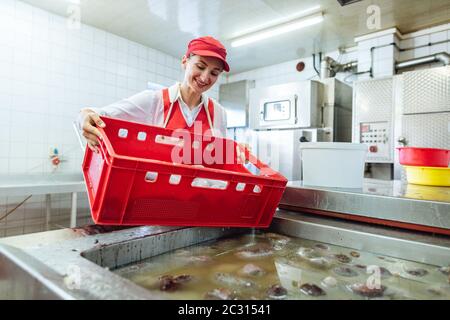 Frau, die in der Metzgerei arbeitet, um Würstchen in heißem Wasser zu kochen, indem sie in den Kessel Stockfoto