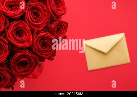 Liebesbrief und Blumenlieferservice am Valentinstag, luxuriöser Strauß roter Rosen und Kartenumschläge auf rotem Hintergrund Stockfoto