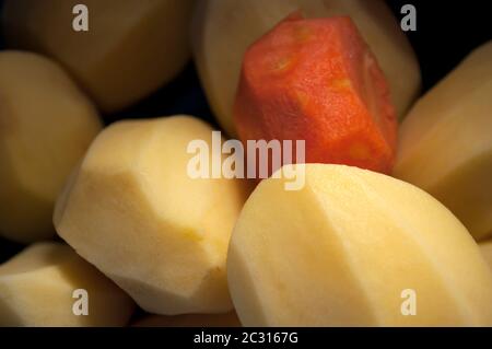 Geschälte Kartoffeln und eine geschälte Karotte aus nächster Nähe, Hintergrund der Speisen. Sonnenlicht fällt in die Mitte des Fotos, der Rest im Schatten.Draufsicht Stockfoto