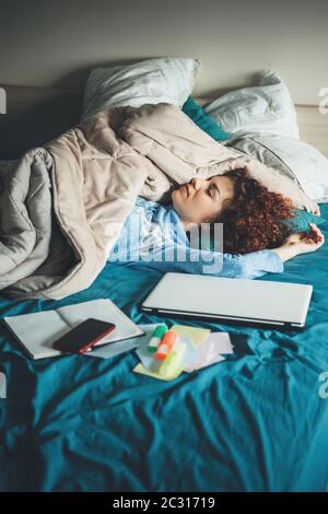 Schlafende kaukasische Frau ruht sich nach Hausaufgaben am Laptop im Bett mit einem Deckchen bedeckt und trägt Pyjamas Stockfoto