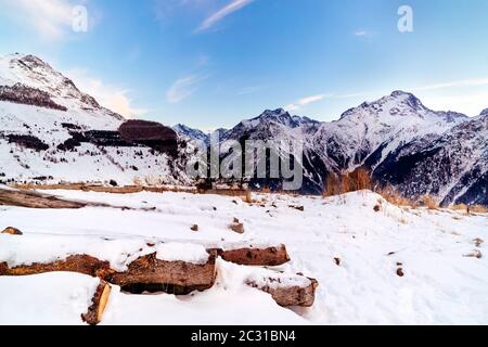 Blick vom Stadtrand von Les deux Alpes Dorf auf Bergkette mit Baumstämmen mit Schnee bedeckt Stockfoto