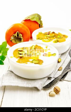Dessert Joghurt, Dattel und Honig mit Vanille, Kardamom und Pistazien in zwei Schalen auf einem Handtuch, Minze und Löffel auf dem Hintergrund der hellen Holzmöbeln boa Stockfoto