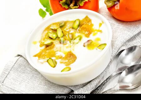 Dessert Joghurt, Dattel und Honig mit Vanille, Kardamom und Pistazien in einer Schüssel auf einem Handtuch, Minze und Löffel auf Holzbrett Hintergrund Stockfoto