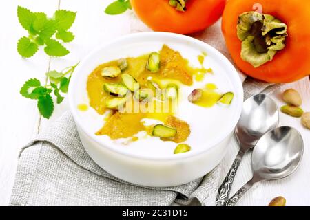 Dessert Joghurt, Dattel und Honig mit Vanille, Kardamom und Pistazien in einer Schüssel auf eine Serviette, Minze und Löffel auf dem Hintergrund des Lichts Holzbrett Stockfoto