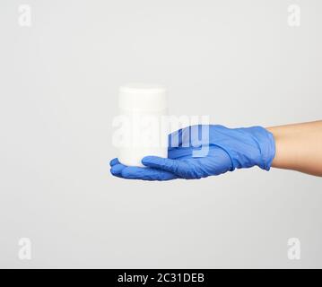 Hand in blau steriler Handschuh hält weißen Plastikbecher mit Pillen auf weißem Hintergrund, nah oben Stockfoto