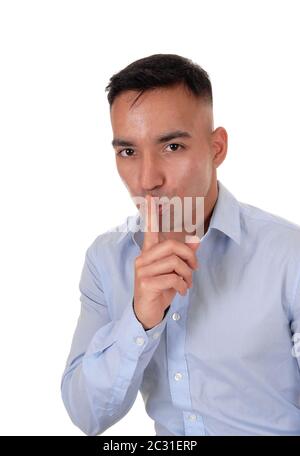 Eine Nahaufnahme Bild einer jungen indischen Mann in ein blaues T-Shirt mit seinem Finger über seinen Mund, sprechen Sie nicht, isoliert für weissen Hintergrund Stockfoto