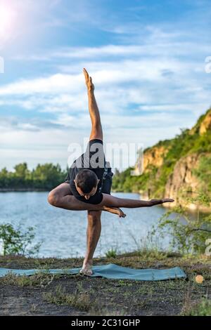 Ein gut aussehender junger bärtiger Mann, der Yoga vor der Kulisse des Steinbruchs macht. Konzept des Internationalen Tages des Yoga. Stockfoto