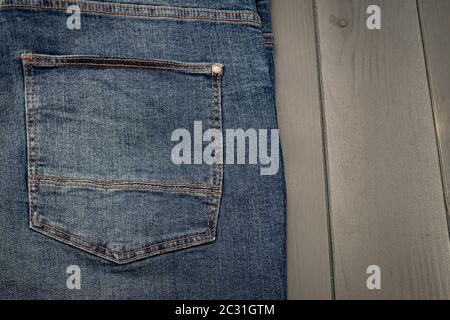 Rückentasche einer gewaschenen blauen Denimhose mit Goldnähten auf grauem Holzhintergrund Stockfoto