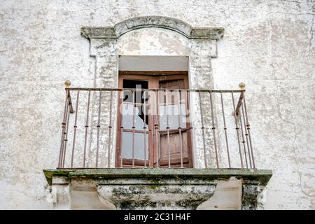 Fenster mit Zugang zu altem Balkon und schmiedeeisernem Zaun, das im Laufe der Zeit an einer Fassade eines alten und rustikalen Hauses schmiedet wurde Stockfoto