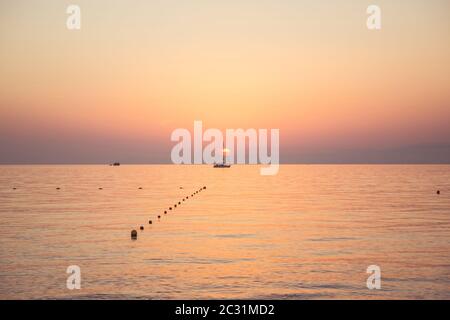 Ein Segelboot segelt bei Sonnenuntergang. Das Boot mitten in der Sonne. Der Himmel und die sind rosa und Gold. Thassos Island, Griechenland Stockfoto