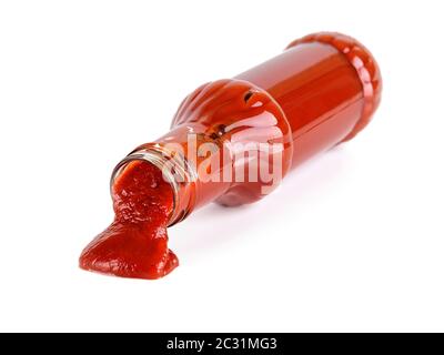 Schmackhaftes dickes Tomatenketchup fließt langsam aus einer Glasflasche, die auf ihrer Seite isoliert auf weißem Hintergrund liegt. Gewürze, Gewürze und Saucen. Stockfoto