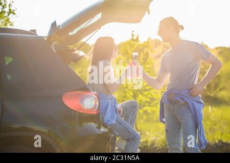 Schöne junge von einem Paar mit romantischen Zeit trinken Getränke im Kofferraum auf den Sonnenuntergang Stockfoto