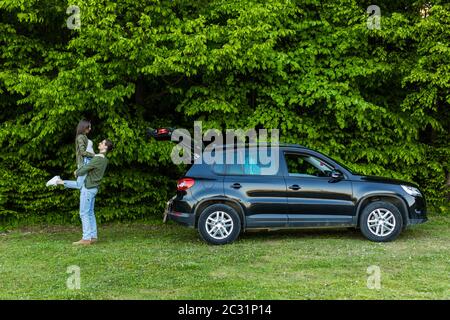 Junges Paar Piggy-Unterstützung Gefühle Zuneigung Leidenschaft Spaß Freizeit in der Nähe Auto im Park Stockfoto