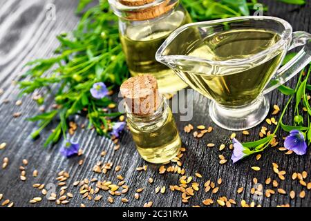 Leinöl in zwei Gläser und eine Sauciere mit Samen, Blätter und Flachs Blumen auf Holzbrett Hintergrund Stockfoto