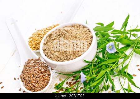 Leinsamen Mehl in eine Schüssel geben, weiße und braune Bettwäsche Samen in zwei Löffel und am Tisch, Blättern und blauen flaxen Blumen auf Holzbrett Hintergrund Stockfoto