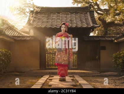 Maiko in einem Kimono, der auf einem Steinweg vor dem Tor eines traditionellen japanischen Hauses posiert Stockfoto