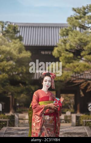 Maiko in einem Kimono, der in Kyoto auf einer Steinbrücke vor dem Tor eines japanischen Tempels posiert Stockfoto