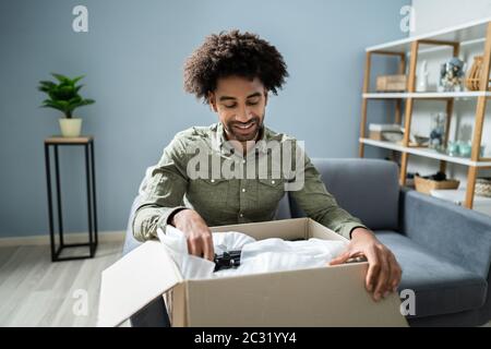 Lächelnden jungen Mann sitzt auf einem Sofa Auspacken empfangene Paket Stockfoto
